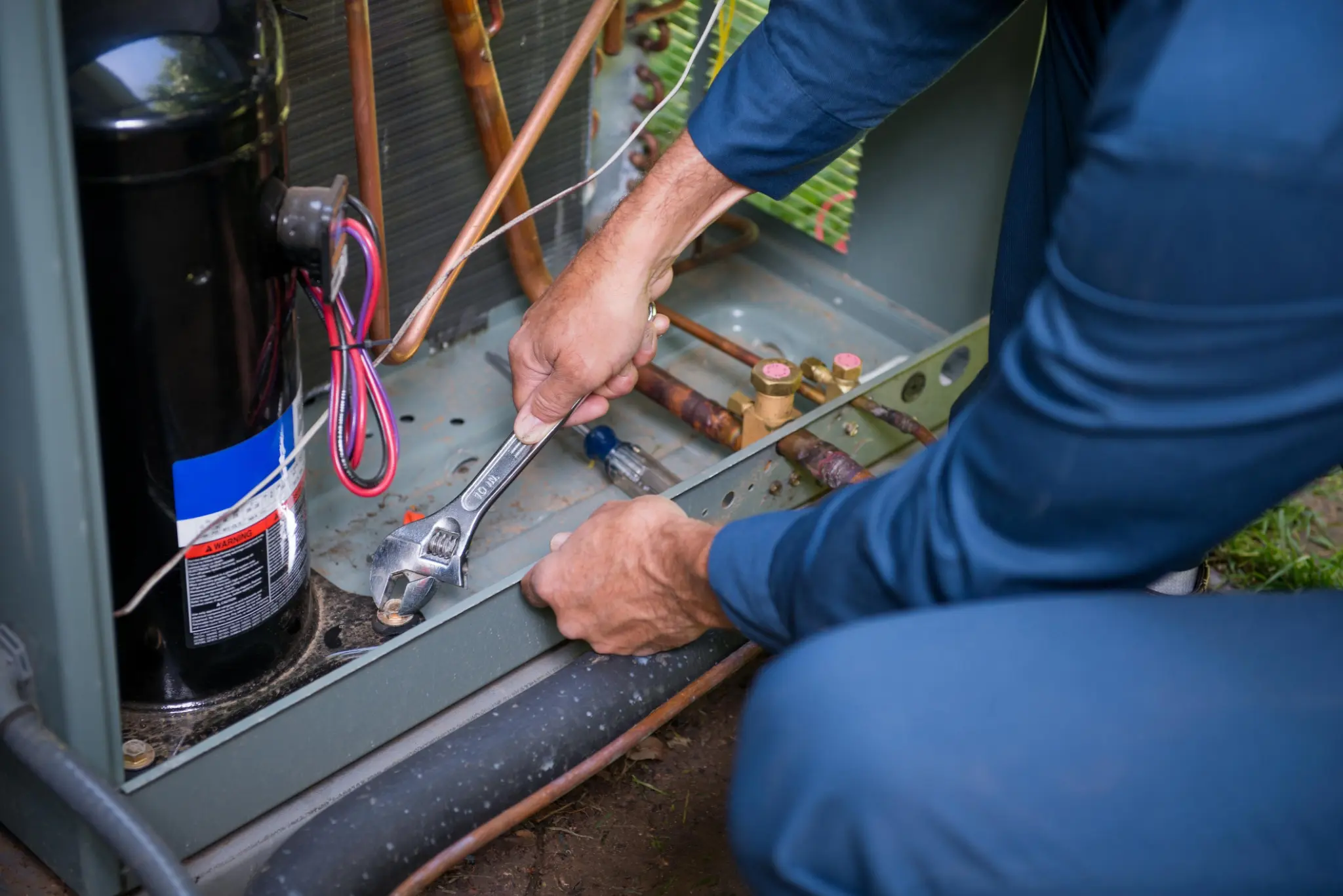 Technician tightening a component inside an outdoor AC condenser