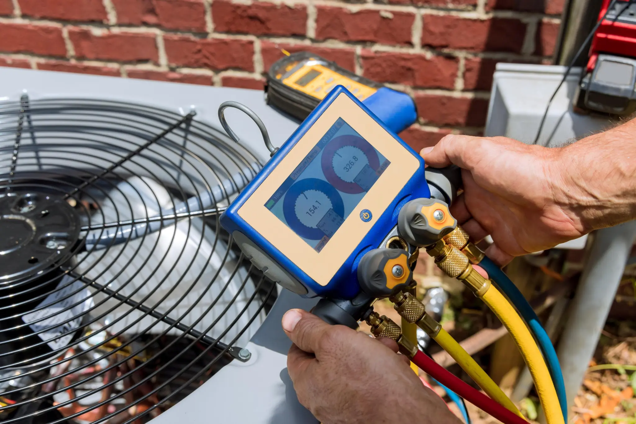 Technician using digital HVAC gauges beside an outdoor condenser